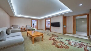 Ein modernes Hotelzimmer mit einer Couch, Sesseln, einem Couchtisch, einem Flachbildfernseher und einem gemusterten Teppich.