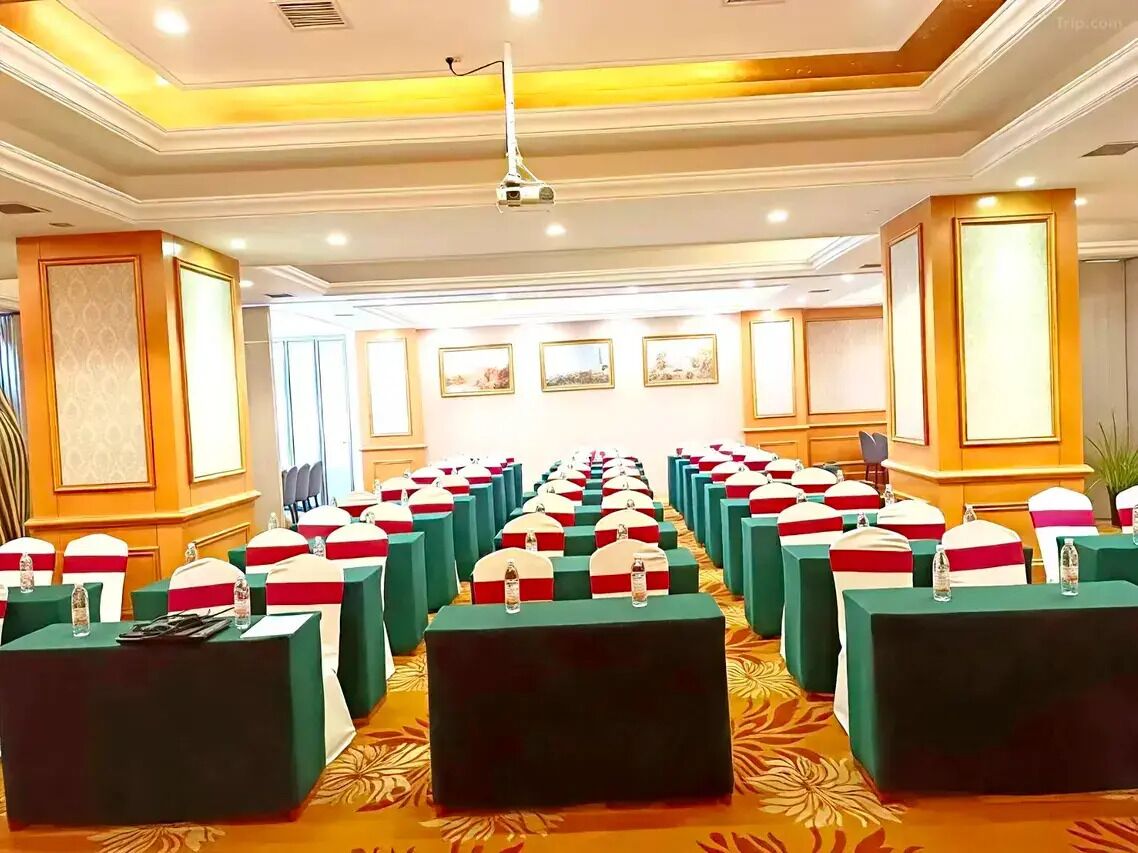 A conference room with rows of tables and chairs, a podium, and framed pictures on the walls.