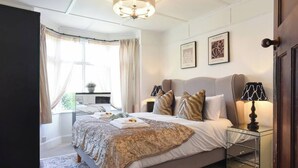 Un dormitorio con cama, mesitas de noche, lámpara y ventana con cortinas.