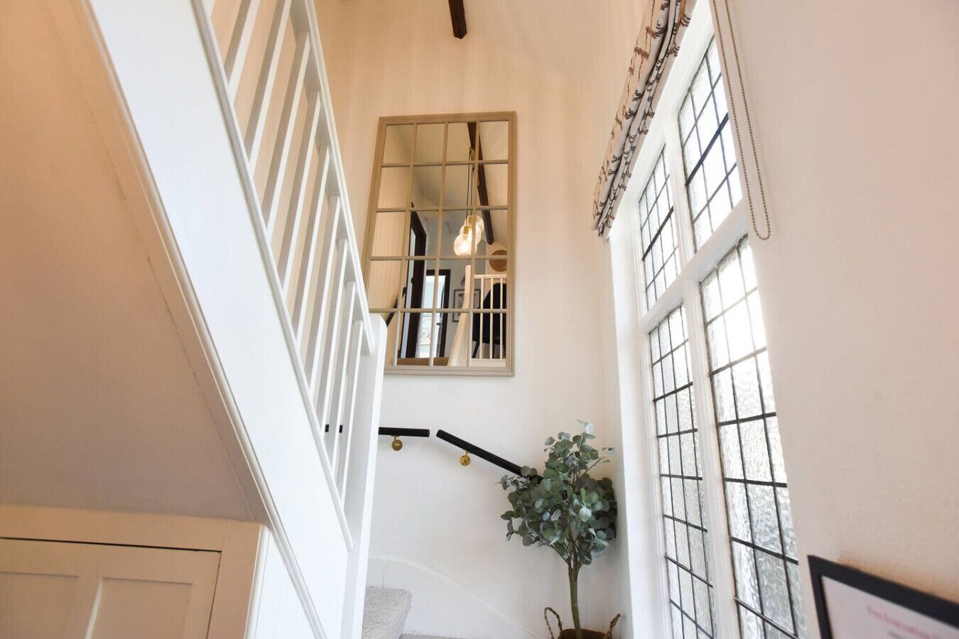 A staircase with a white railing, a potted plant, and a window with a grid pattern.