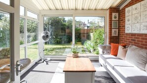 Una habitación luminosa con puerta de vidrio corredera, un ventilador, un sofá blanco y una mesa de madera.