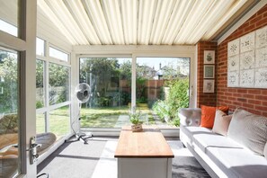 A sunlit room with a sliding glass door, a fan, a white sofa, and a wooden table. - ✨Parc Avenue – A Charming Stay in the Heart of Cosham, Portsmouth! ✨ (Cosham)