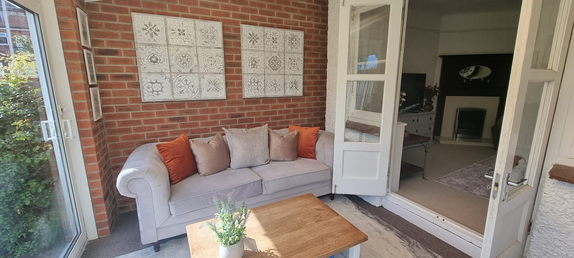 A room with a brick wall, a white sofa with orange cushions, a wooden coffee table, and a door leading to another room.