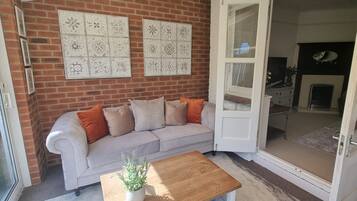 A room with a brick wall, a white sofa with orange cushions, a wooden coffee table, and a door leading to another room.