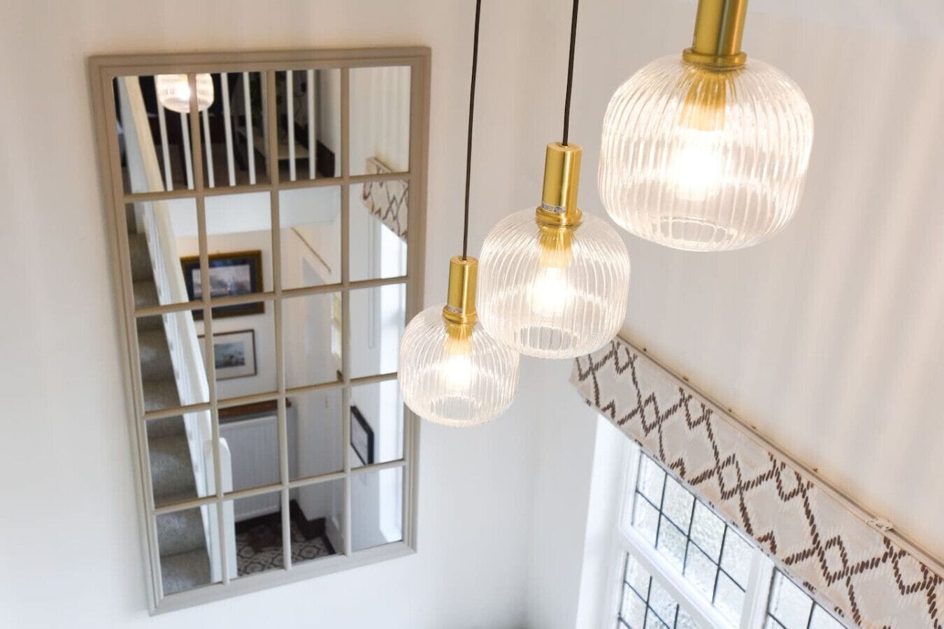 A staircase with a mirrored wall, three hanging pendant lights, and patterned wall trim.