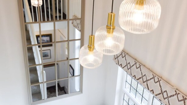 Una escalera con un muro espejado, tres lámparas colgantes y molduras decorativas en la pared.