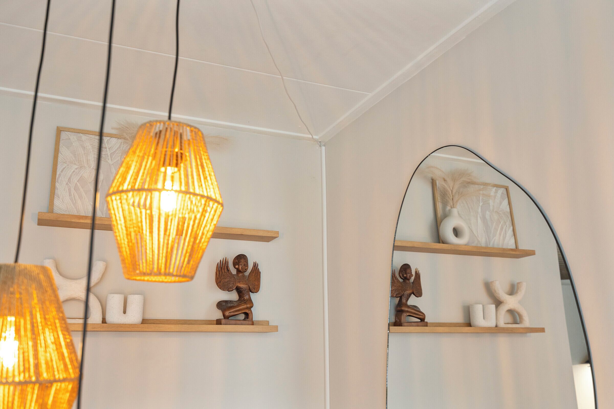 Een kamer met houten planken waarop decoratieve objecten staan, een grote spiegel en hangende lampen.