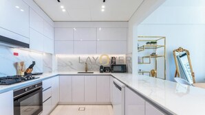 A modern kitchen with white cabinetry, a stainless steel stove, and a microwave. - Layover Holiday Homes (Dubai)