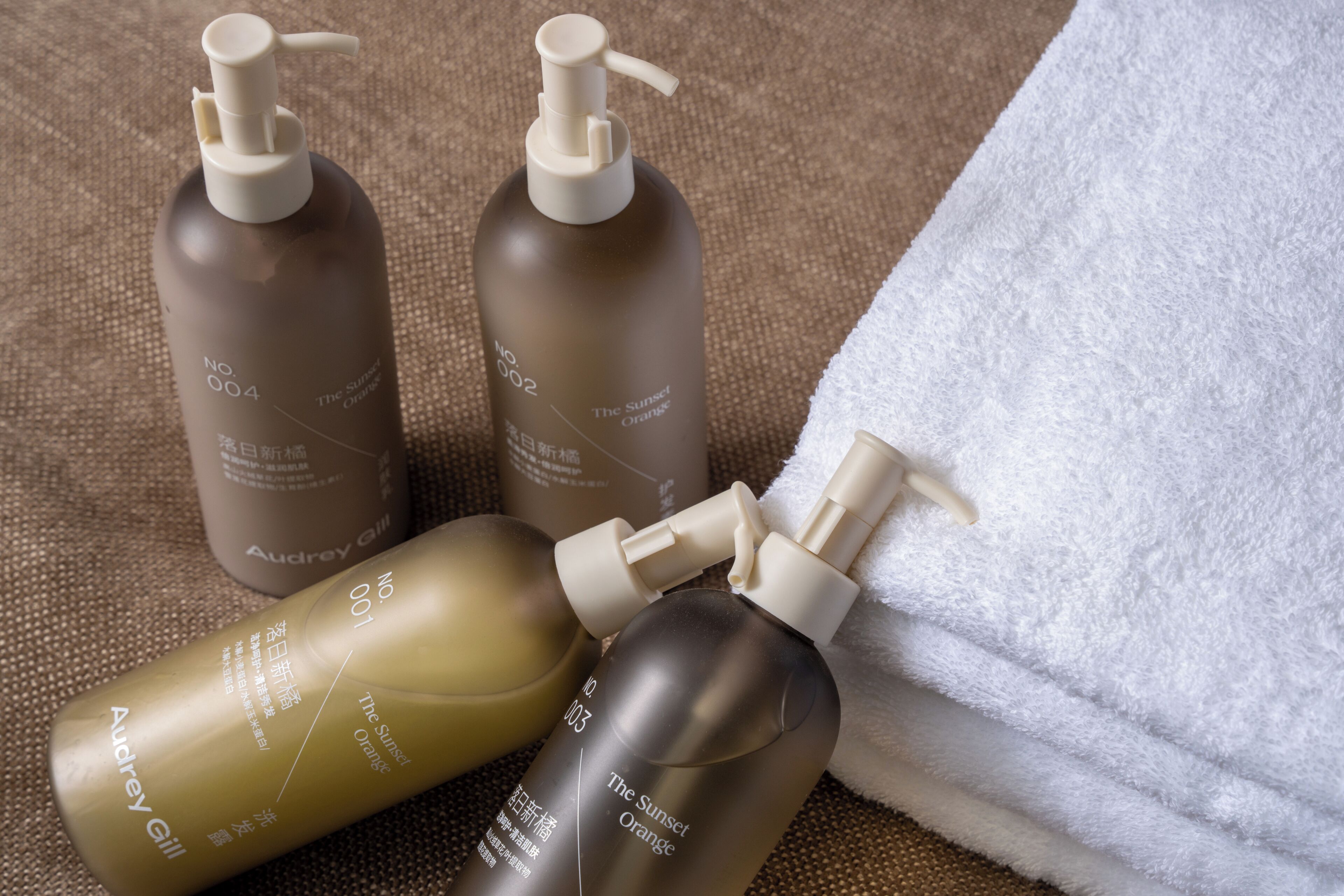 Three bottles of skincare products with pumps, a white towel, and a textured fabric surface.