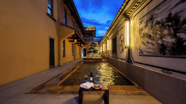 A narrow alleyway with a water feature, a table with a bottle and glass, and traditional architecture.