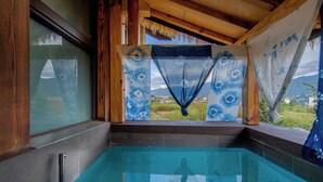 A swimming pool with a view of a mountainous landscape, wooden beams, and a thatched roof.