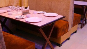 A dining area with a table set for four, cushioned seating, and a small table with a tissue box and glasses. - Hotel Shar Inn (Balrampur)