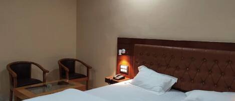Habitación de hotel con una cama, dos sillas, una mesita de noche con teléfono y una lámpara fijada a la pared.