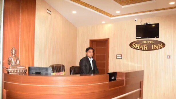 A hotel reception desk with a wooden finish, a Buddha statue, a television mounted on the wall, and a sign that reads 'Hotel Shar Inn'. - Hotel Shar Inn (Balrampur)