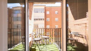 Un balcon avec une petite table et des chaises, une clôture en métal et une vue sur un immeuble en briques.
