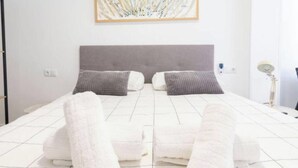Un lit bien fait, avec des oreillers et des serviettes pliées, une lampe de chevet et un tableau encadré au mur.