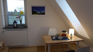 Una habitación acogedora con techo inclinado, una mesa con lámpara, un radiador y una ventana con vistas.