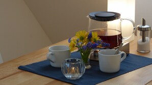 Una mesa con una cafetera, dos tazas, un vaso y un jarrón con flores.