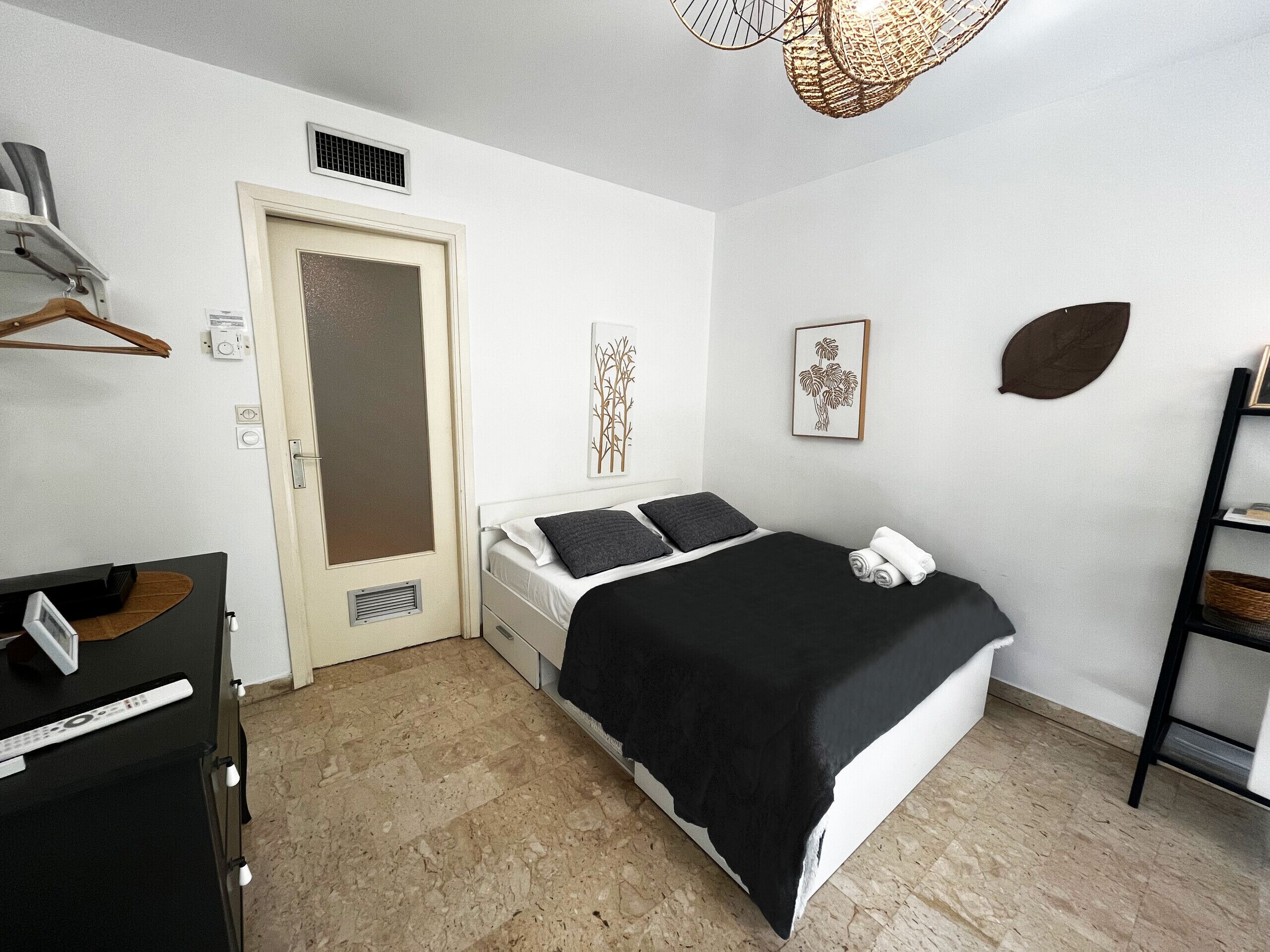 A bedroom with a bed, a desk, a chair, a wardrobe, a door, and a shelf with a plant.