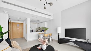 A modern living room with a sofa, a dining table, chairs, a TV, and a kitchen area in the background. - Silkhaus Premium 2BR in Reem Island in Radiant Bay (Abu Dhabi)