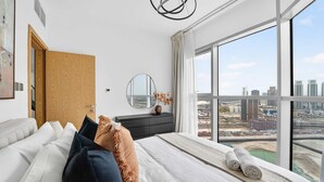 A modern hotel room with a large bed, a wooden door, a round mirror, and a view of the cityscape. - Silkhaus Premium 2BR in Reem Island in Radiant Bay (Abu Dhabi)