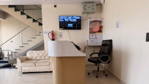 Egy recepciós pult, mögötte egy kanapé és egy szék, egy lépcsőház, és egy a falra szerelt televízió.