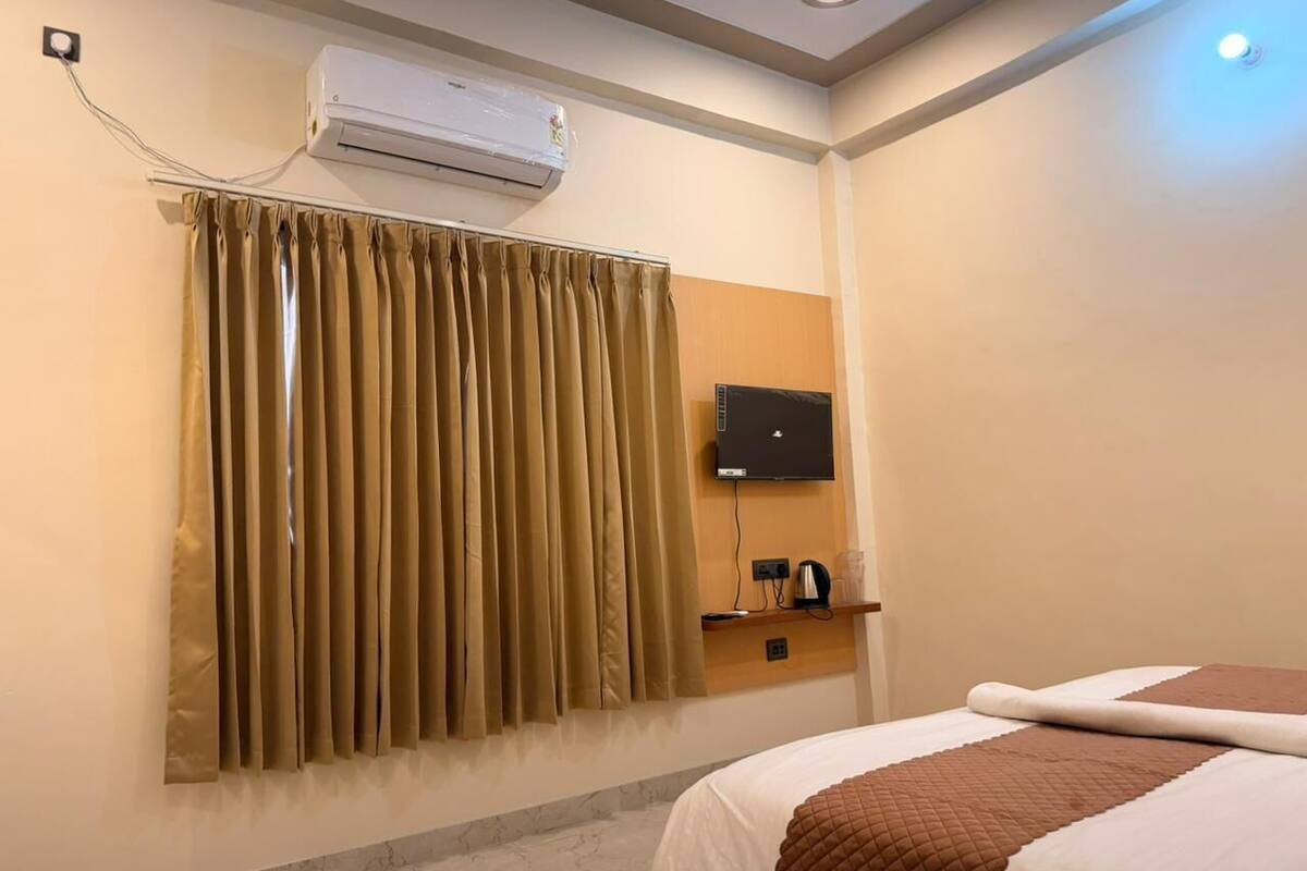 Una habitación de hotel con cama, aire acondicionado, televisor y un pequeño estante con un hervidor.