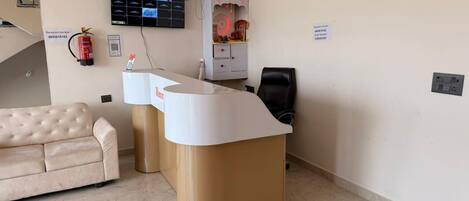 A reception desk with a digital display, a fire extinguisher, a sofa, and a chair.