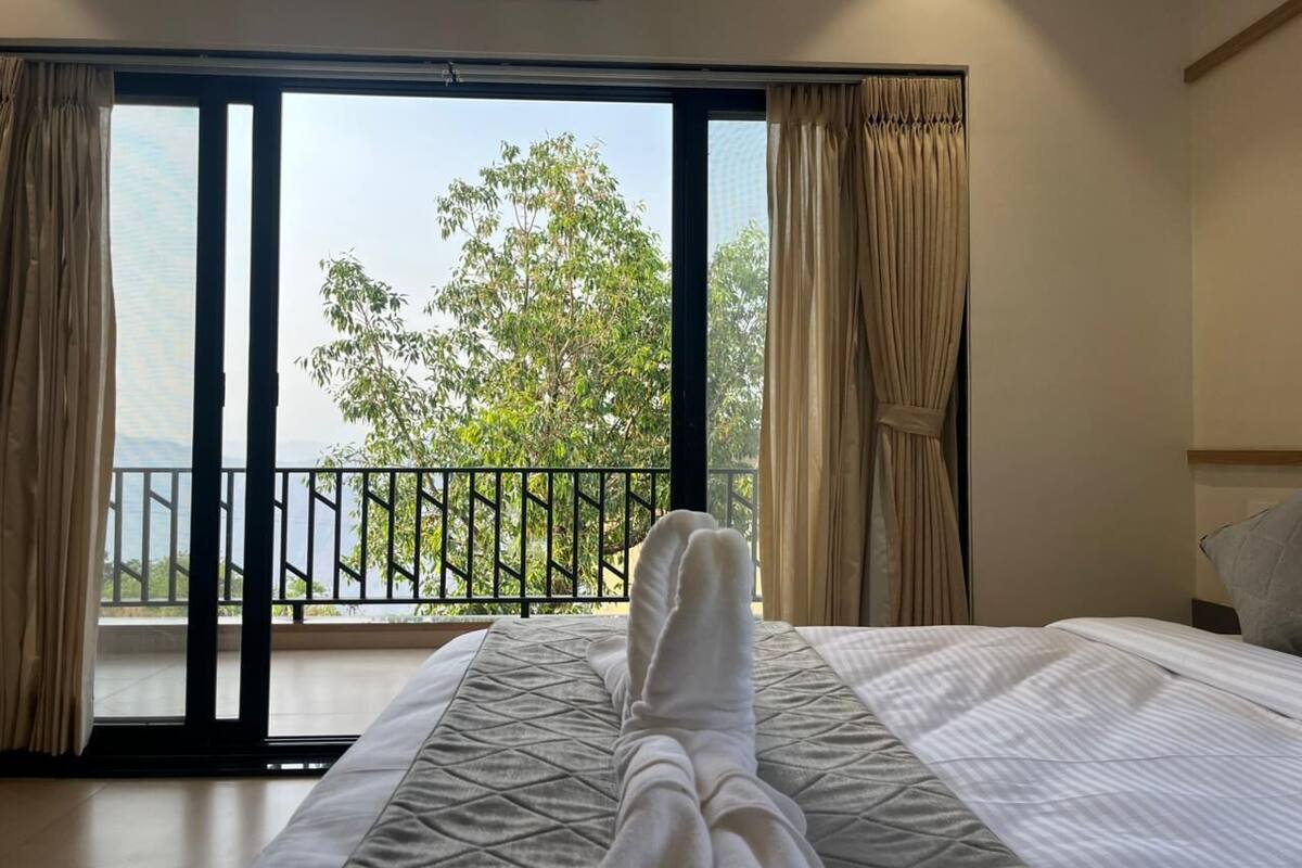 Quarto com cama, cortinas e vista para uma varanda com guarda-corrimão.