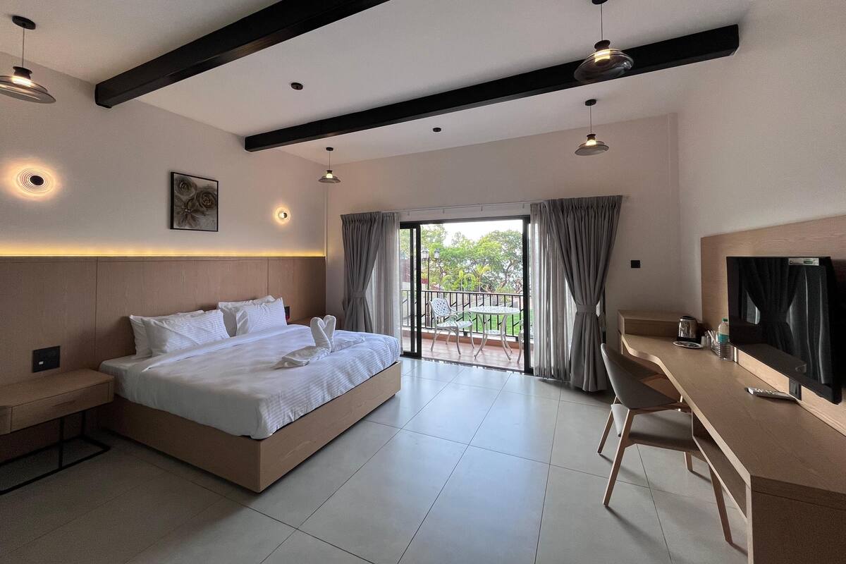 Quarto de hotel moderno com cama grande, escrivaninha e varanda com cortinas.