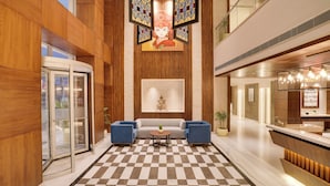 A lobby with a checkered floor, a reception desk, a sofa, and a glass elevator. - Lemon Tree Premier Biratnagar Nepal (Biratnagar)