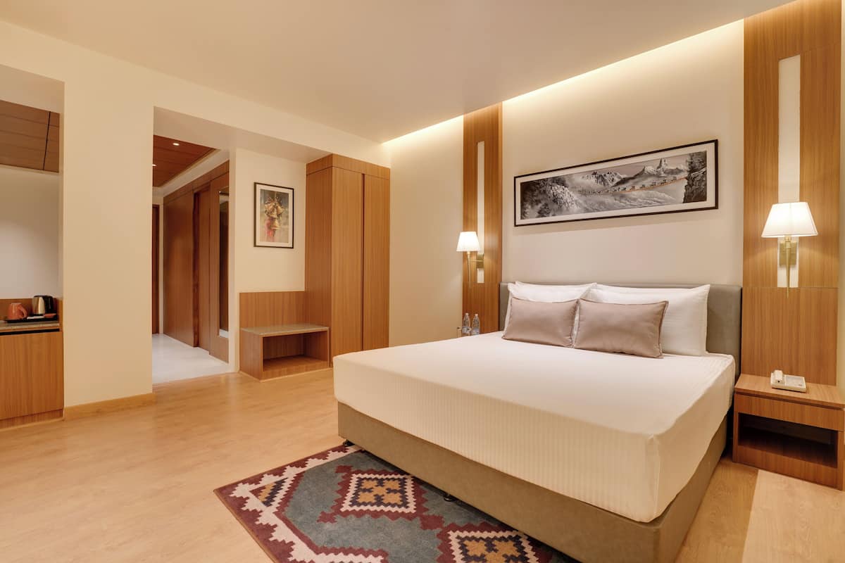 Una habitación de hotel con una cama grande, lámparas de noche, un cuadro en la pared y un armario de madera.