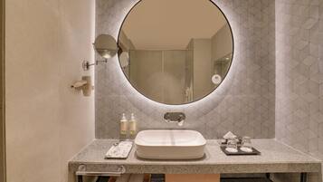 Casa de banho com espelho redondo, lavatório e suporte de toalhas.