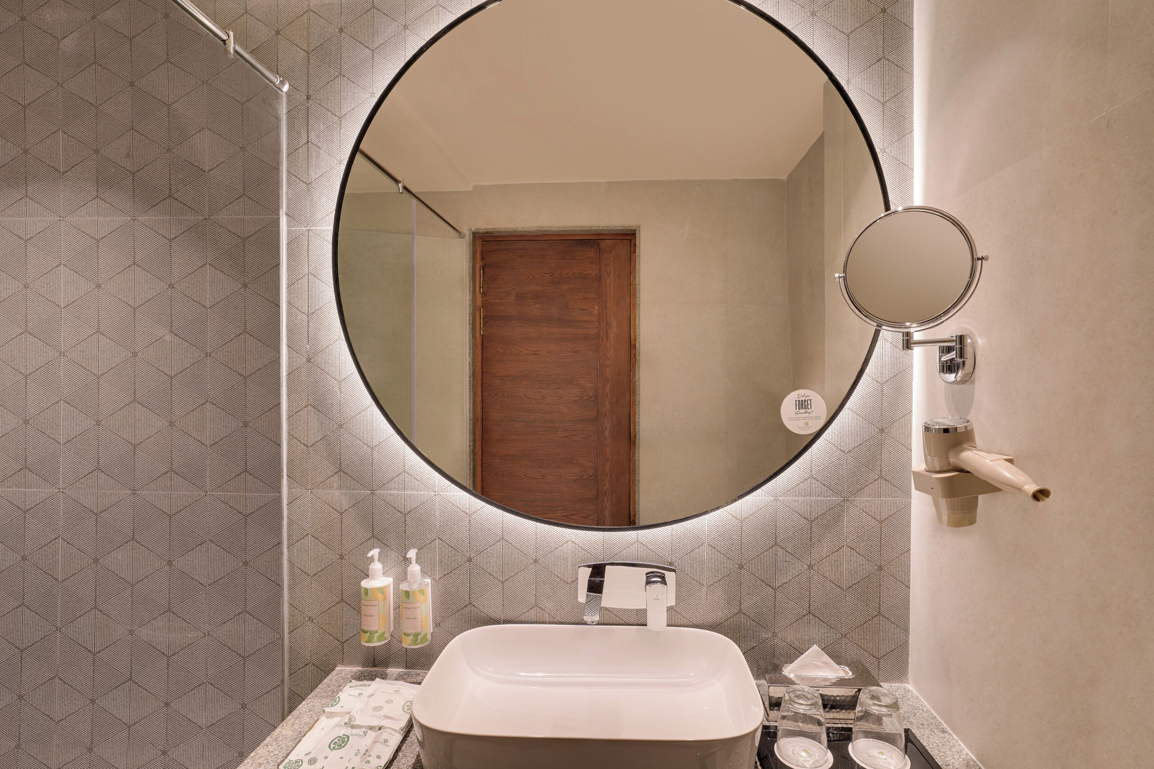 A bathroom with a round mirror, a wooden door, a sink, and toiletries.