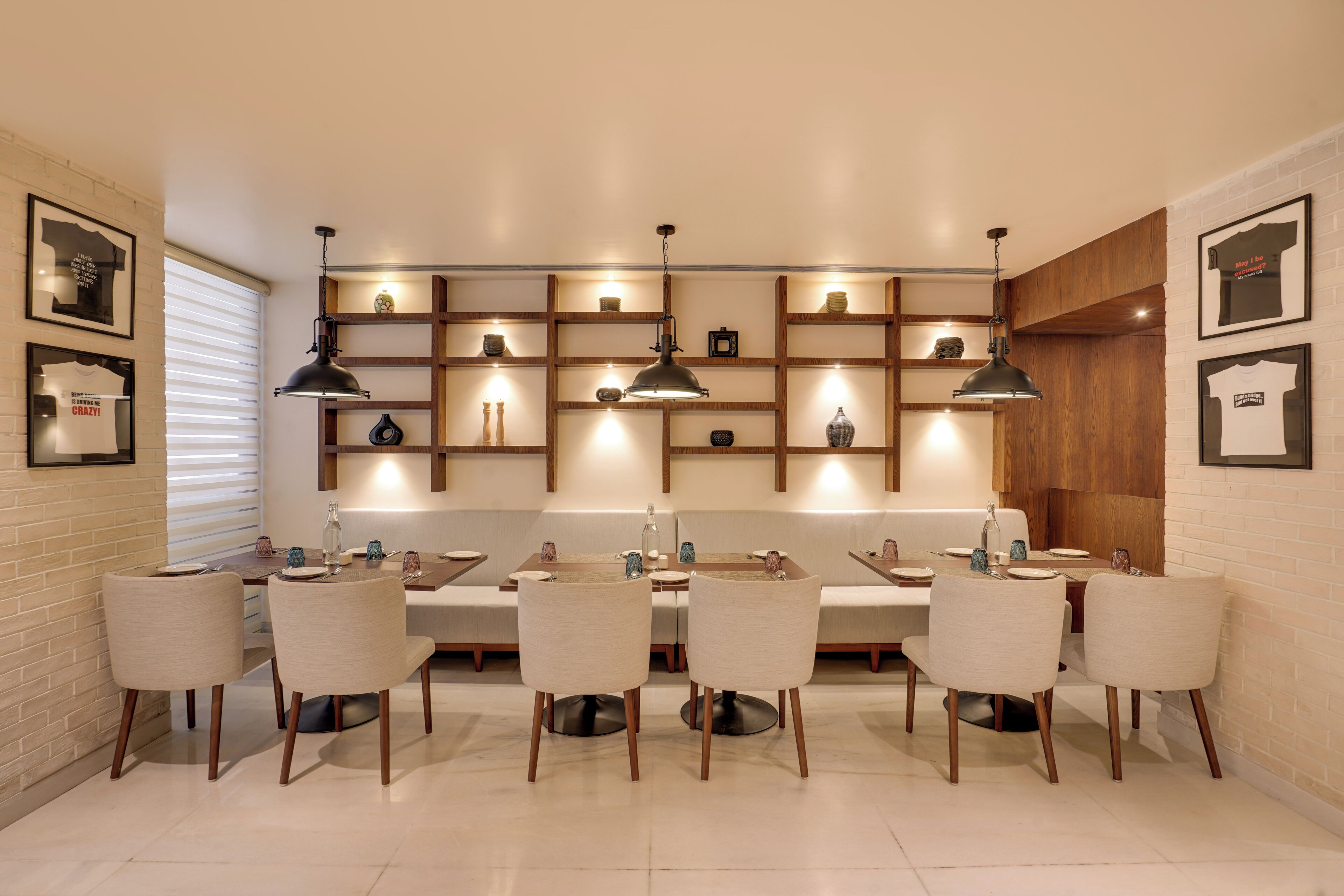 Un espace repas comprenant une longue table, des chaises, des luminaires suspendus et des étagères ornées d’objets décoratifs.