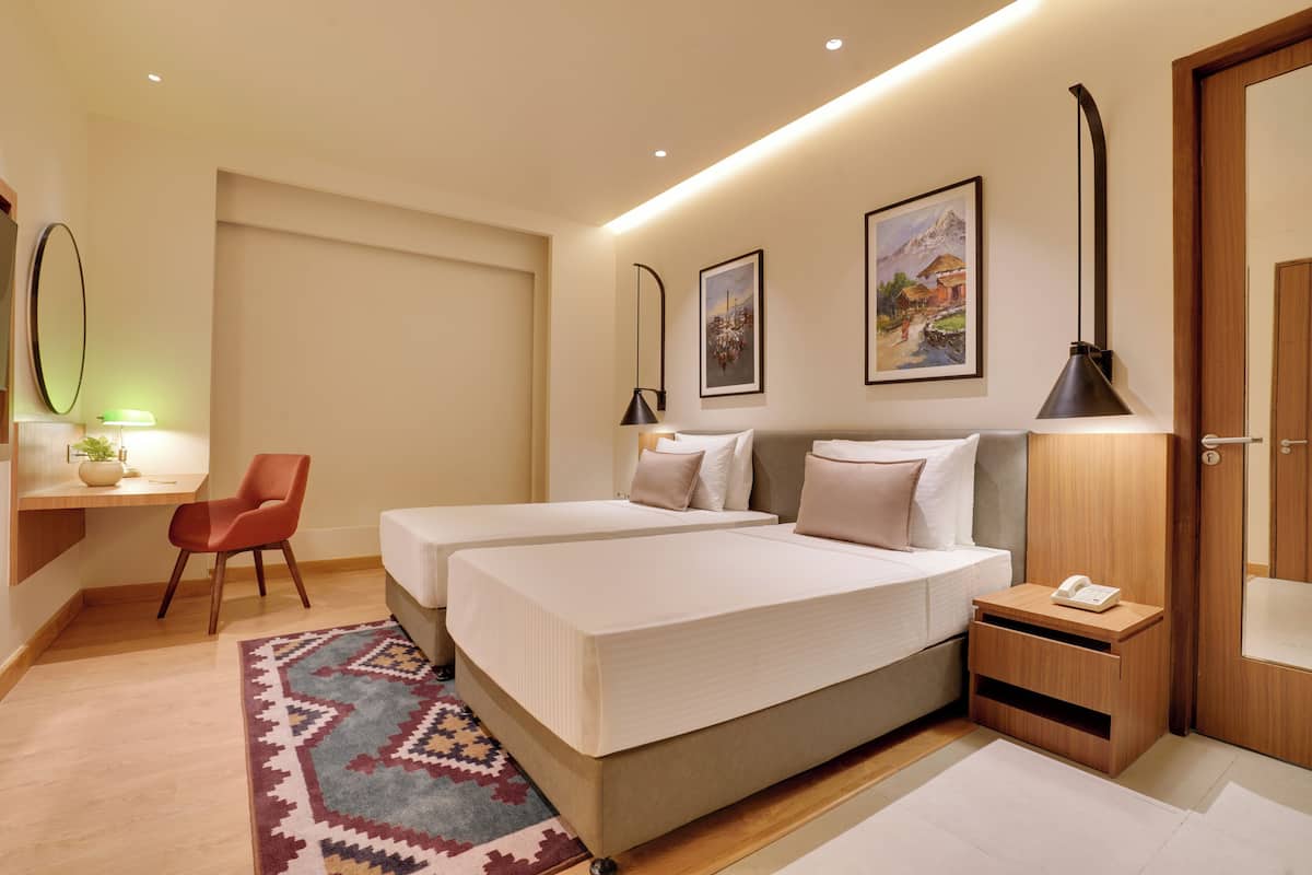 Habitación de hotel con dos camas, un escritorio, una silla, una mesita de noche y obras de arte en las paredes.