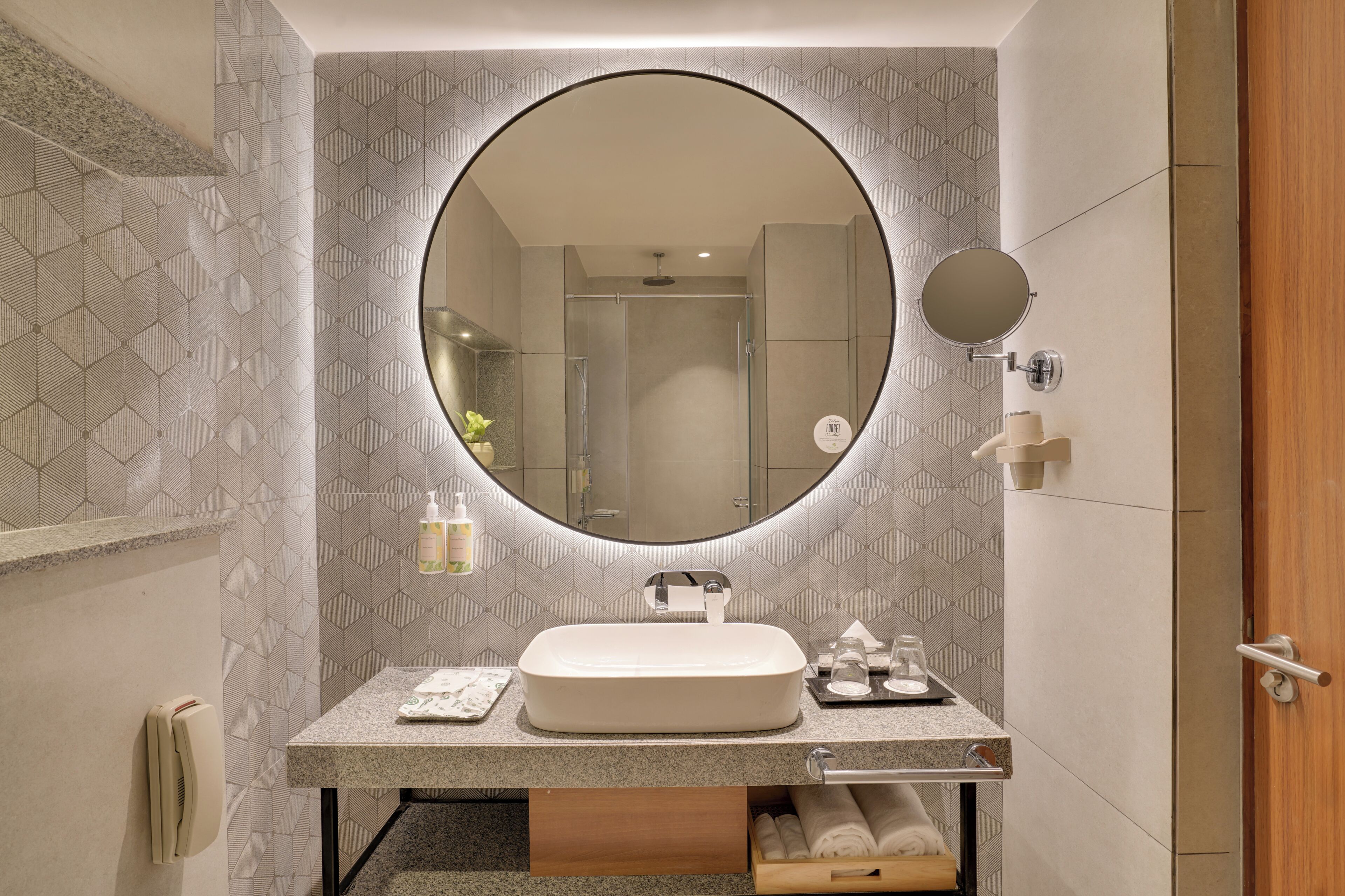 Un baño con espejo redondo, lavamanos, toallero y zona de ducha.