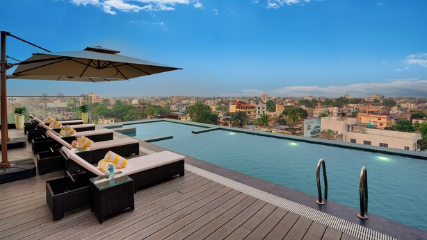 A rooftop pool with lounge chairs and an umbrella, overlooking a cityscape. - Lemon Tree Premier Biratnagar Nepal (Biratnagar)