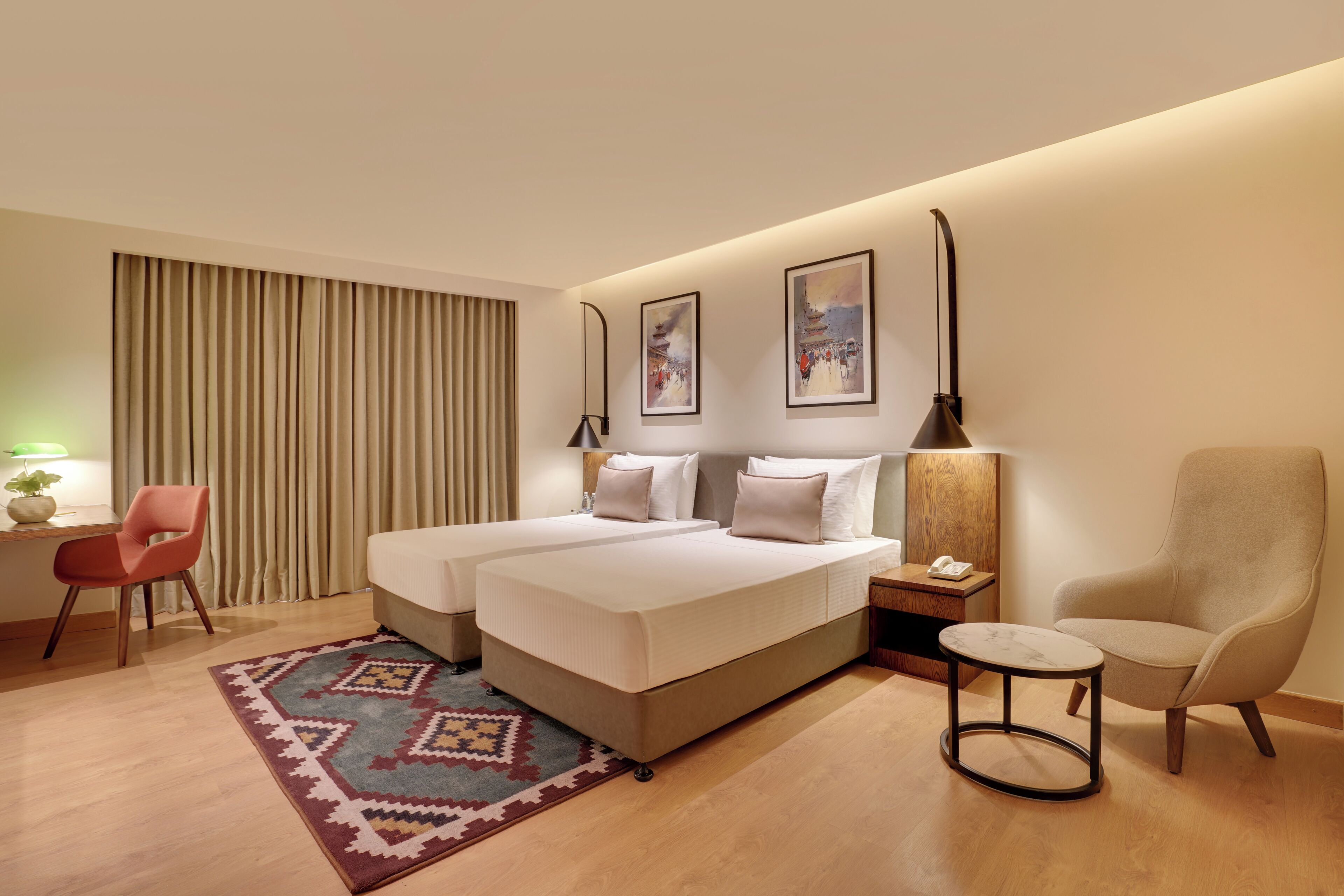 Una habitación de hotel con cama, dos mesitas de noche, una silla, un escritorio, una lámpara y una alfombra.