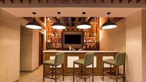 A bar area with a brick wall, wooden ceiling beams, and pendant lighting. There are three bar stools and a flat-screen TV mounted on the wall. - Lemon Tree Premier Biratnagar Nepal (Biratnagar)