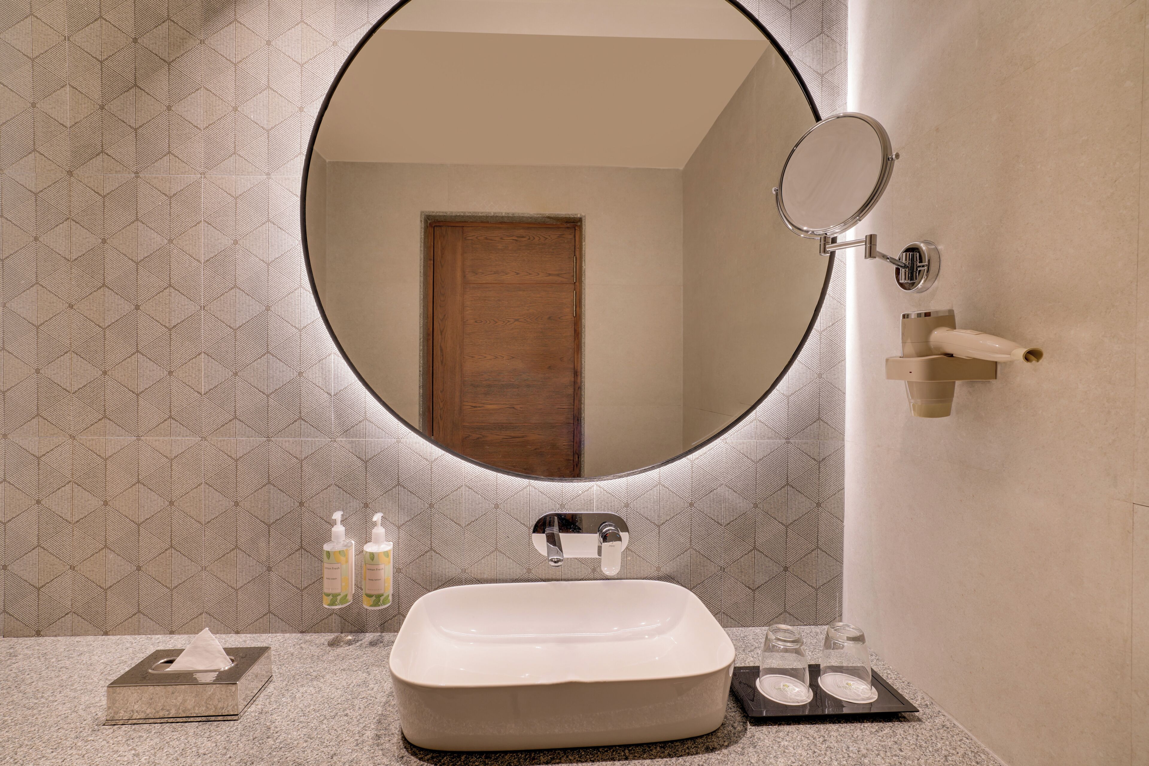 Un baño con un espejo redondo, un lavabo blanco y un perchero para toallas.
