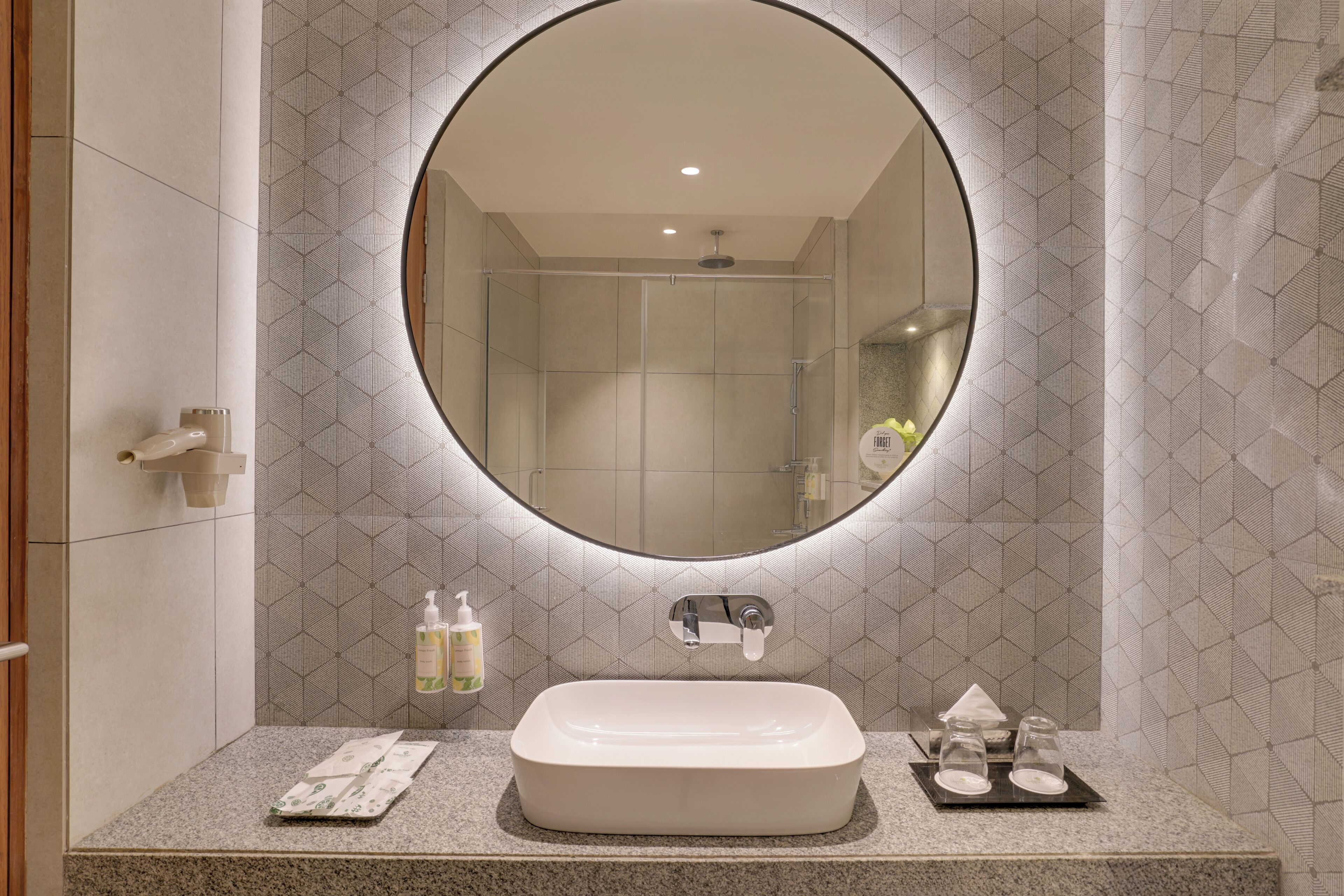 A bathroom with a rectangular sink, a round mirror, and a shower area.