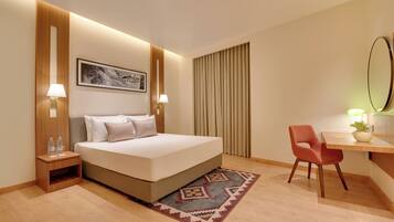 Habitación de hotel con cama, lámparas de noche, escritorio con silla, planta en maceta y un espejo grande.