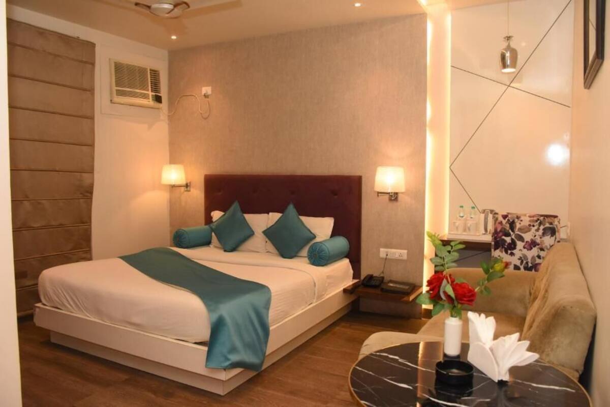 A hotel room with a bed, bedside lamps, a nightstand, a small table with a vase of flowers, and a couch.