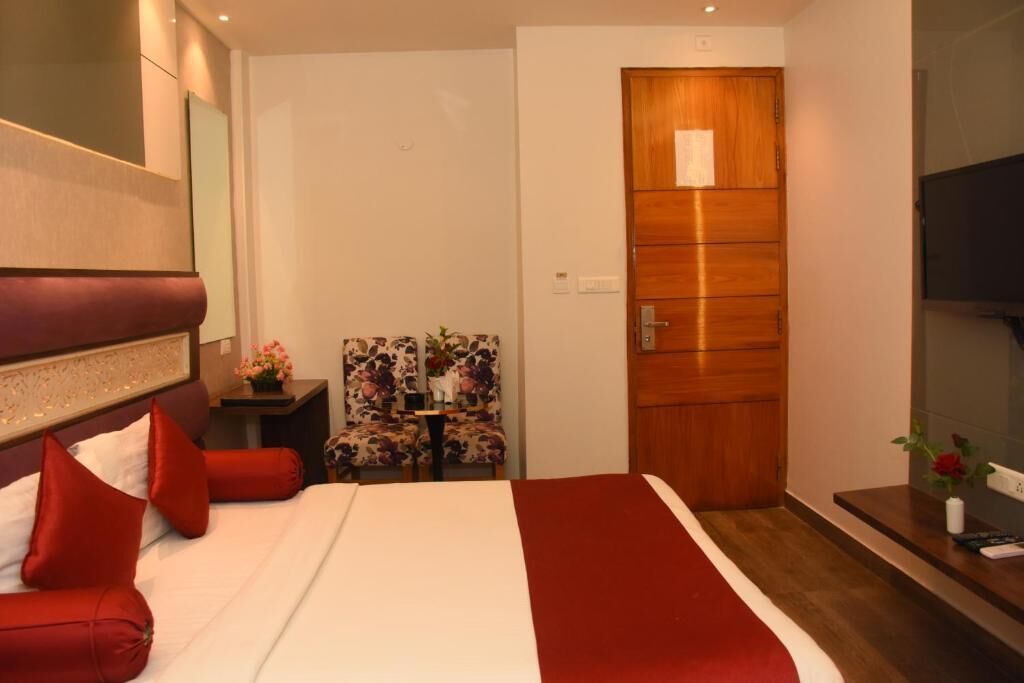 Habitación de hotel con cama, una puerta de madera, una silla y una mesita con un florero.