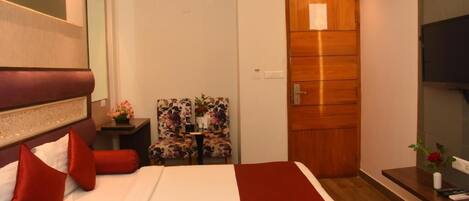 Habitación de hotel con cama, una puerta de madera, una silla y una mesita con un florero.