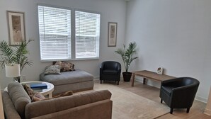 Una sala de estar con un sofá, un sillón, una mesa de centro y dos plantas en macetas.