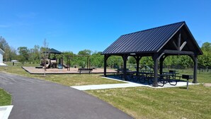 Un parque con un pabellón, mesas para picnic, un parque infantil y un sendero pavimentado.