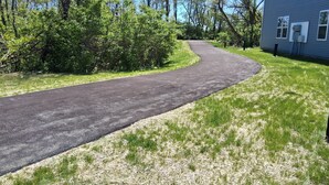 Un camino de entrada pavimentado que serpentea alrededor de una casa con césped y árboles.