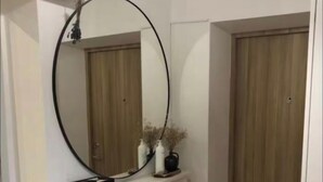 Een hal met een witte dressoir, een ronde spiegel en een houten deur.